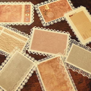 May include: Assortment of decorative paper cards with lace trim. The cards are in various colours and textures, including brown, beige, and pink.