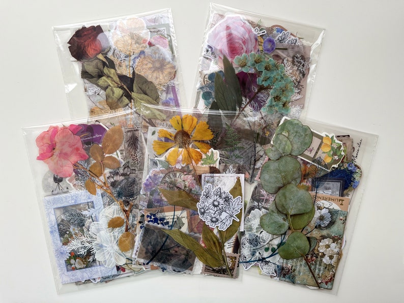 Op de afbeelding: Vier doorzichtige plastic zakjes gevuld met geperste bloemen- en bladstickers. De stickers tonen een verscheidenheid aan bloemendesigns, waaronder rozen, madeliefjes en eucalyptusbladeren. De stickers zijn perfect om een vleugje natuur toe te voegen aan je knutselwerk en projecten.