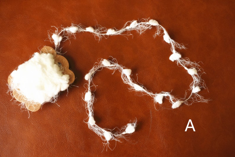 May include: A white fluffy garland with small pom poms. The garland is on a brown surface. The letter A is written on the surface.