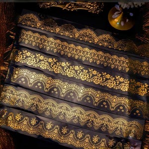 May include: A collection of decorative gold lace ribbons with intricate floral and geometric patterns. The ribbons are arranged on a dark background, creating a contrast that highlights the gold details. The image showcases the variety of designs available.
