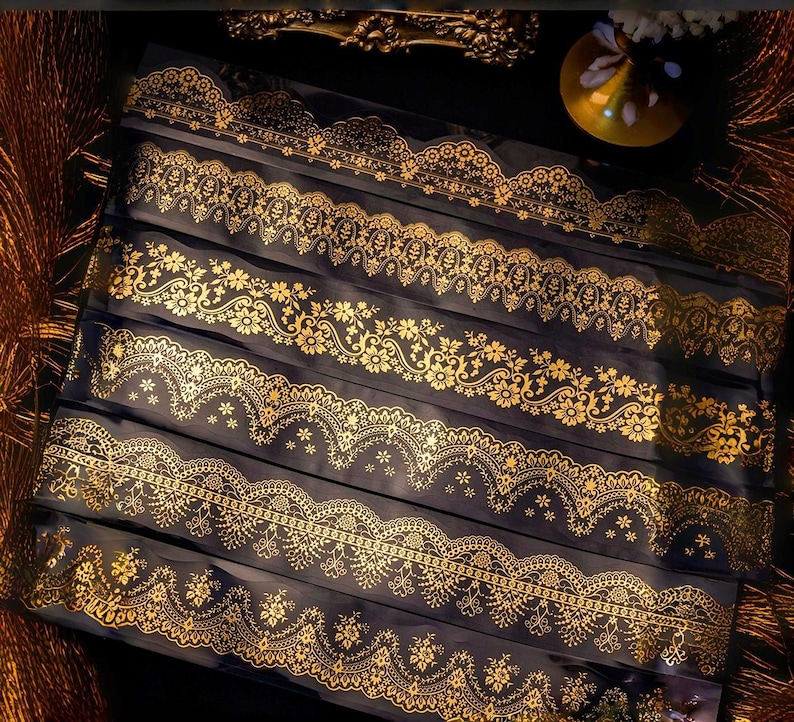 Op de afbeelding: Een verzameling gouden kanten linten met gedetailleerde bloemen- en geometrische patronen. De linten zijn gerangschikt op een donkere achtergrond, waardoor de gouden details worden benadrukt. De afbeelding toont de verscheidenheid aan beschikbare ontwerpen.