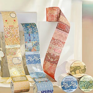 Può includere: Rotoli di nastro adesivo washi decorativo con motivi floreali e botanici. Il nastro presenta disegni con fiori, motivi botanici ed etichette di testo. I rotoli sono etichettati "Maurice's Flower Paper" e includono la frase "have a good day."