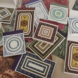 May include: A collection of small, square notebooks with decorative covers. The covers feature intricate patterns in various colours, including blue, green, red, and gold. Each notebook has a different design.