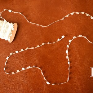 May include: A spool of white trim with a brown cardboard spool. The trim is laid out in a curved shape on a brown leather surface. The letter "I" is written in white on the surface.