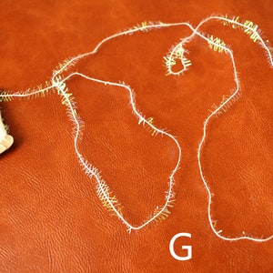 May include: A spool of white and gold tinsel with a small amount of tinsel unraveled on a brown surface. The letter "G" is written on the surface.