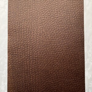 May include: A rectangular sheet of brown faux leather with a textured surface. The word "Brown" is written in a cursive font at the bottom of the sheet. The background is a white floral pattern.