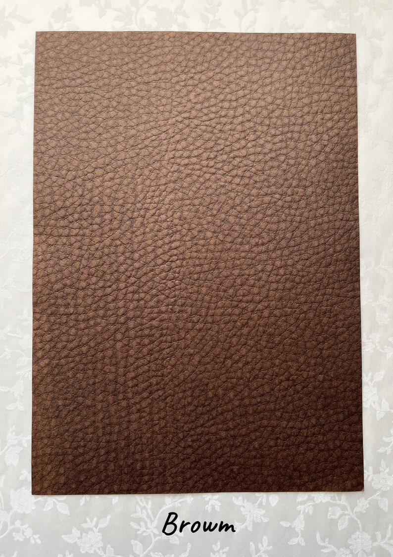May include: A rectangular sheet of brown faux leather with a textured surface. The word "Brown" is written in a cursive font at the bottom of the sheet. The background is a white floral pattern.
