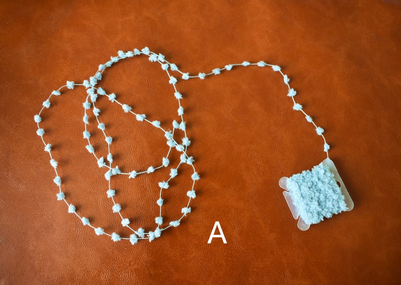 May include: A spool of light blue fuzzy trim with a small amount of trim already unwound. The trim is made of small, fluffy balls.