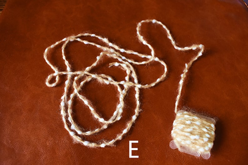 May include: A ball of brown and white yarn with white flecks. The yarn is on a brown leather surface. The letter "E" is written below the yarn.