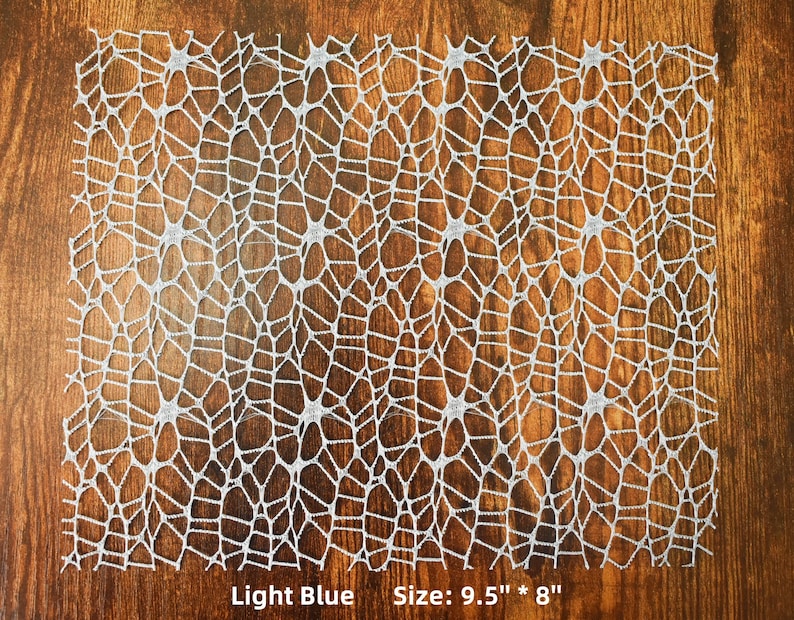 Op de afbeelding: Een lichtblauwe kant tafelkleed met een delicaat web-achtig patroon. Maat: 9,5" x 8"