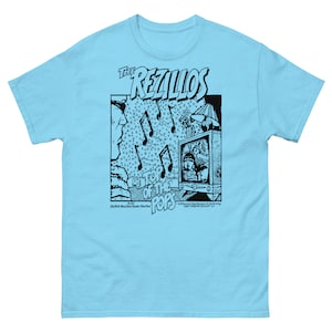 May include: A light blue t-shirt with a black and white graphic print of a band called "The Rezillos" with the text "Top of the Pops" and "20,000 Rezillos Under The Sea".