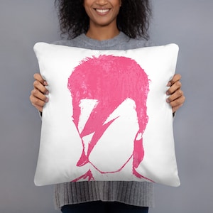 May include: A white pillow with a pink silhouette of David Bowie's face with a lightning bolt across his eye.