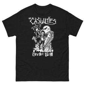 May include: Black t-shirt featuring a white graphic of a skeleton holding a coffin and a spray can. The text "The Casualties" and "Never Die" is printed on the shirt.