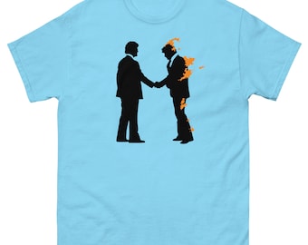 May include: Light blue t-shirt featuring a black silhouette of two men shaking hands, with orange flames emanating from one figure. The design is centered on the front of the shirt, offering a striking visual contrast.