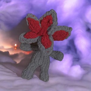 May include: A grey plush toy with a red flower on its head. The toy is standing on a white surface with a purple background.