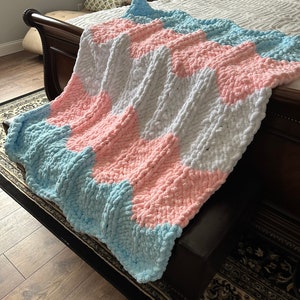 May include: A soft, chunky knit blanket with a chevron pattern in shades of light blue, pink, and white.