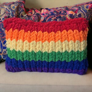 Puede incluir: Una almohada de crochet de colores arco&iacute;ris con una superficie texturizada. La almohada est&aacute; hecha de hilo rojo, naranja, amarillo, verde, azul y morado.