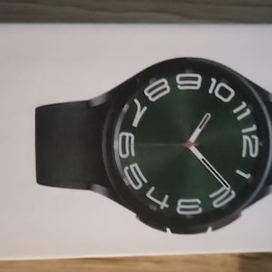 Peut inclure: Une montre connectée noire avec un cadran vert et des chiffres blancs. La montre a un bracelet noir.