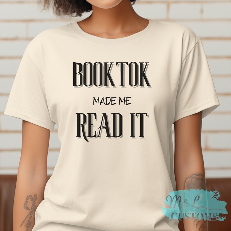 Puede incluir: Una camiseta blanca con texto negro que dice "BookTok Made Me Read It".