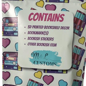 May include: A white resealable bag with a pink and purple bookshelf design. The bag contains a 3D printed bookshelf decor, bookmark(s), bookish stickers, and other bookish items. The bag also has the text "CONTAINS" and "M&L CUSTOMS".