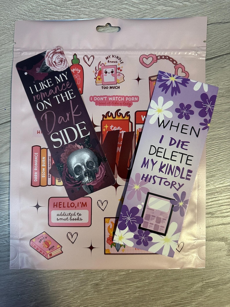 May include: Two purple and white bookmarks with funny sayings. The first bookmark says "I like my romance on the dark side" with a skull and crossbones graphic. The second bookmark says "When I die delete my kindle history".
