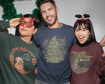 May include: Three people wearing Christmas themed sweatshirts. The person in the middle is wearing a navy blue sweatshirt with the text "In all the places you find love it feels like Christmas". The person on the left is wearing a green sweatshirt with a cartoon sheep wearing a scarf and the text "Please sir, I want some cheese". The person on the right is wearing a maroon sweatshirt with a cartoon character wearing a blue hat and the text "There's magic in the air this evening".