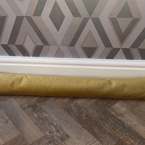 May include: A mustard yellow fabric doorstop. The doorstop is lying on a wooden floor.
