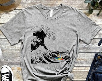 May include: A gray t-shirt with a black and white graphic of a wave with a pug riding a surfboard. The surfboard is rainbow colored.