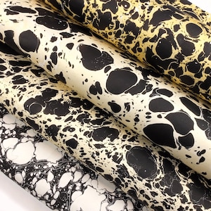 May include: Three rolls of fabric featuring a marbled pattern. The top roll has a gold background with black ink swirls. The middle roll has a cream background with black ink swirls. The bottom roll has a white background with black ink swirls.