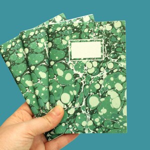 May include: A stack of three green marbled notebooks with a blank label on the front cover.