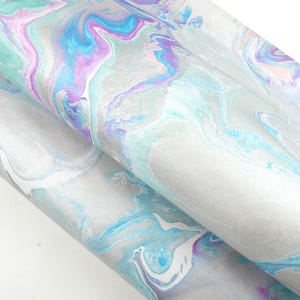 May include: A sheet of fabric featuring a marbled pattern with swirling colours of light blue, bright turquoise, soft purple, and white. The design displays fluid, organic shapes that blend together across the surface, creating a continuous abstract effect.