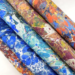 May include: Four sheets of paper featuring a marbled pattern with swirling colours including blue, orange, yellow, purple, and white. The design consists of organic, rounded shapes and intricate veins created through a traditional marbling technique.