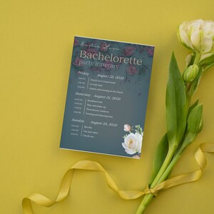 Könnte beinhalten: Eine blaue und weiße Karte mit einem Reiseplan für eine Junggesellinnenabschiedsparty mit floralen Akzenten. Die Karte listet die Daten und Uhrzeiten für die Wochenendaktivitäten auf, darunter Check-in, Frühstück und Spa-Tag.