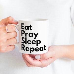 May include: White ceramic mug with black text that reads "Eat Pray Sleep Repeat".
