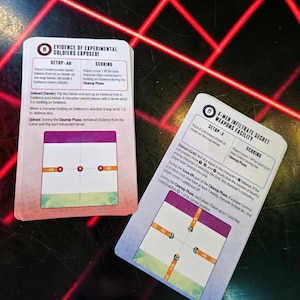 May include: Two game cards are shown, featuring text and illustrations. One card is labelled "EVIDENCE OF EXPERIMENTAL SOLDIERS EXPOSED", the other "X-MEN INFILTRATE SECRET WEAPONS FACILITY". The cards have a colourful design against a red and black background.