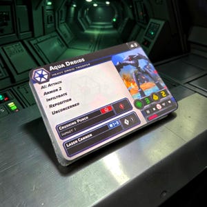 May include: A stack of Aqua Droids Heavy Droid Trooper trading cards. The cards feature a blue and white logo, a futuristic illustration, and game statistics. The text includes "Crushing Punch" and "Laser Cannon". The cards are on a metallic surface.