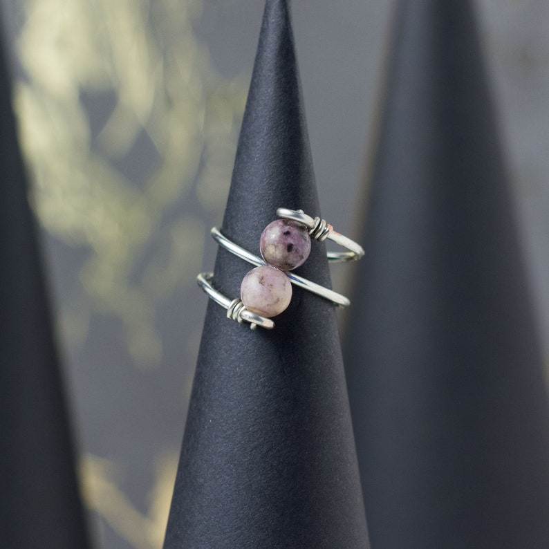 Op de afbeelding: Een zilveren draadring met twee roze en paarse edelsteen kralen.