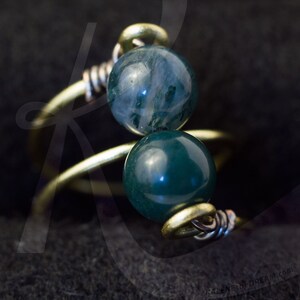 Op de afbeelding: Een gouden draadring met twee groene en blauwe agaat kralen. De kralen zijn rond en hebben een gladde, gepolijste afwerking.