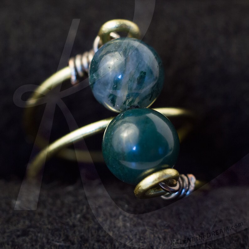 Op de afbeelding: Een gouden draadring met twee groene en blauwe agaat kralen. De kralen zijn rond en hebben een gladde, gepolijste afwerking.