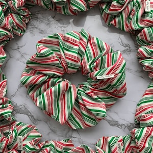 May include: A collection of red and green striped hair scrunchies. The scrunchies are made of fabric and have a white background with red and green stripes.