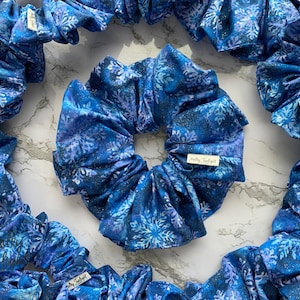 May include: A set of blue and white scrunchies with a snowflake pattern. The scrunchies are made of fabric and have a small white tag with the text "Molly Tuckett" on them.