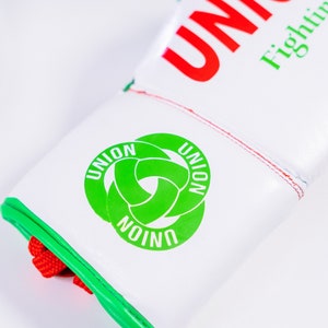 May include: White boxing gloves with red and green trim. The gloves have the word "UNION" written in red on the top and a green logo with the word "UNION" written three times in a circle.