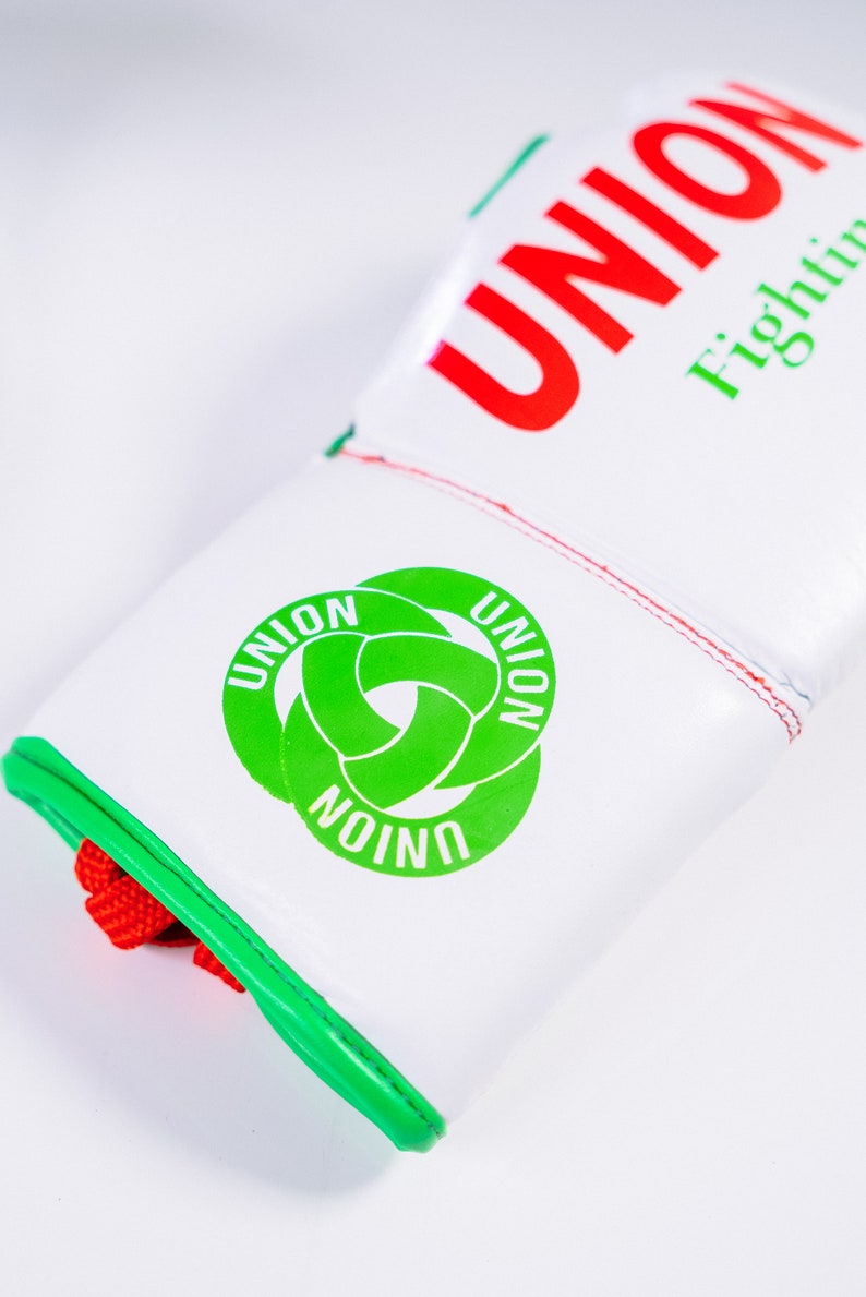 May include: White boxing gloves with red and green trim. The gloves have the word "UNION" written in red on the top and a green logo with the word "UNION" written three times in a circle.