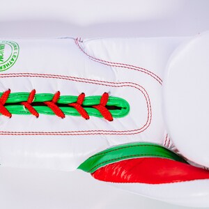 May include: White boxing gloves with red and green accents. The gloves have a lace-up closure and the text "TS1" is printed on the side. The gloves are made of genuine leather.