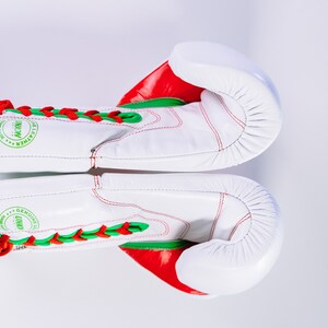 May include: White boxing gloves with red and green accents. The gloves have laces and the text "GENUINE LEATHER" is printed on the side.