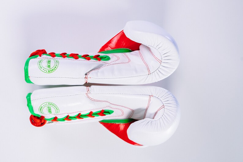May include: White boxing gloves with red and green accents. The gloves have laces and the text "GENUINE LEATHER" is printed on the side.