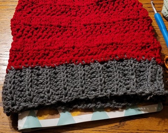 May include: A handmade crochet beanie in red and gray. The top portion is a vibrant red, while the brim is a darker gray. The hat is made with a textured stitch, giving it a cozy appearance. This winter hat is perfect for cold weather.