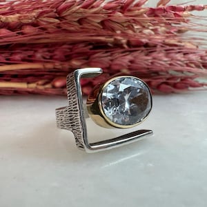 Puede incluir: Un anillo de plata y oro con una gran piedra de cristal transparente engastada en un dise&ntilde;o geom&eacute;trico.