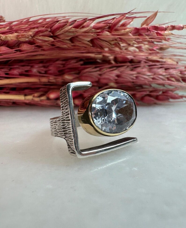 Puede incluir: Un anillo de plata y oro con una gran piedra de cristal transparente engastada en un dise&ntilde;o geom&eacute;trico.