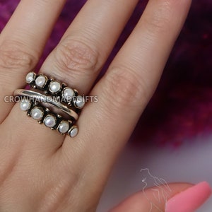 May include: A silver ring with a double row of white pearls. The ring is on a finger with pink nail polish.